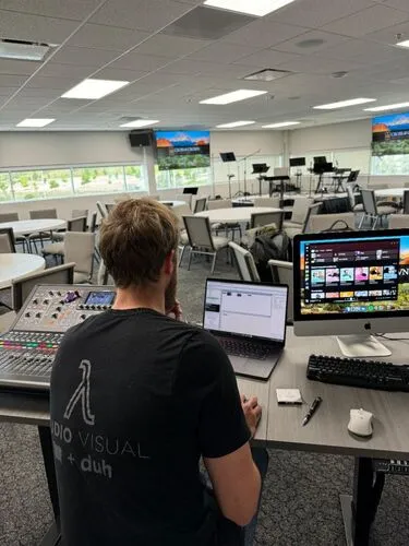 Technician setting up audio and visual equipment for an event in a multipurpose room.
