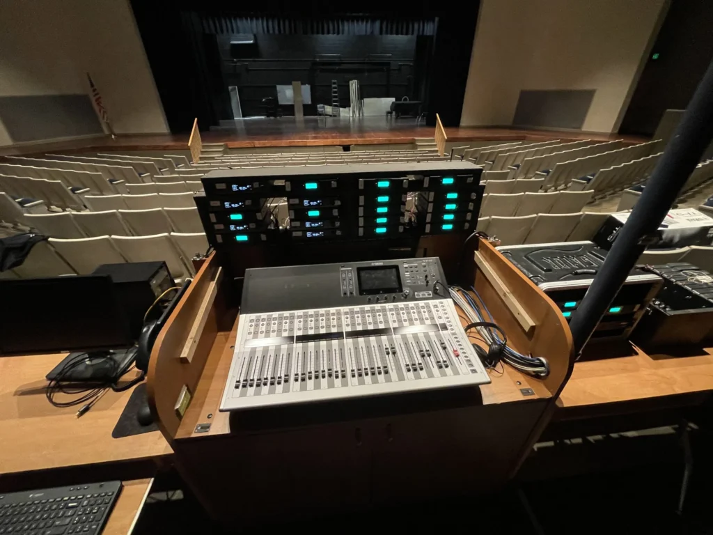 Sound mixing console with rows of empty seats and a stage in the background.