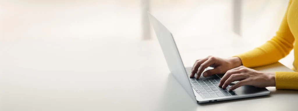 Person wearing a yellow sweater typing on a laptop.