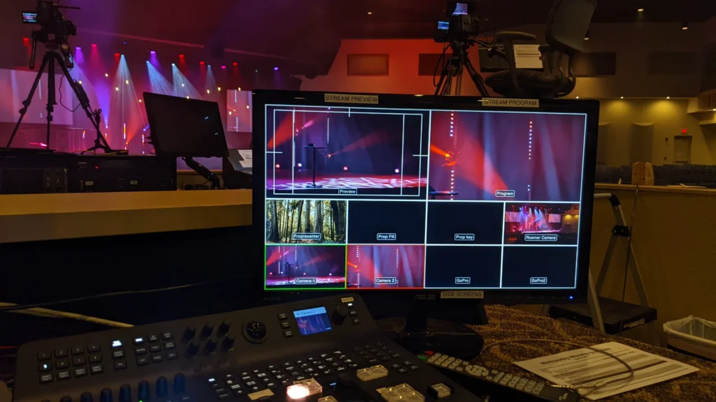 Control room setup with monitors showing live video feed and stage with colorful lights.