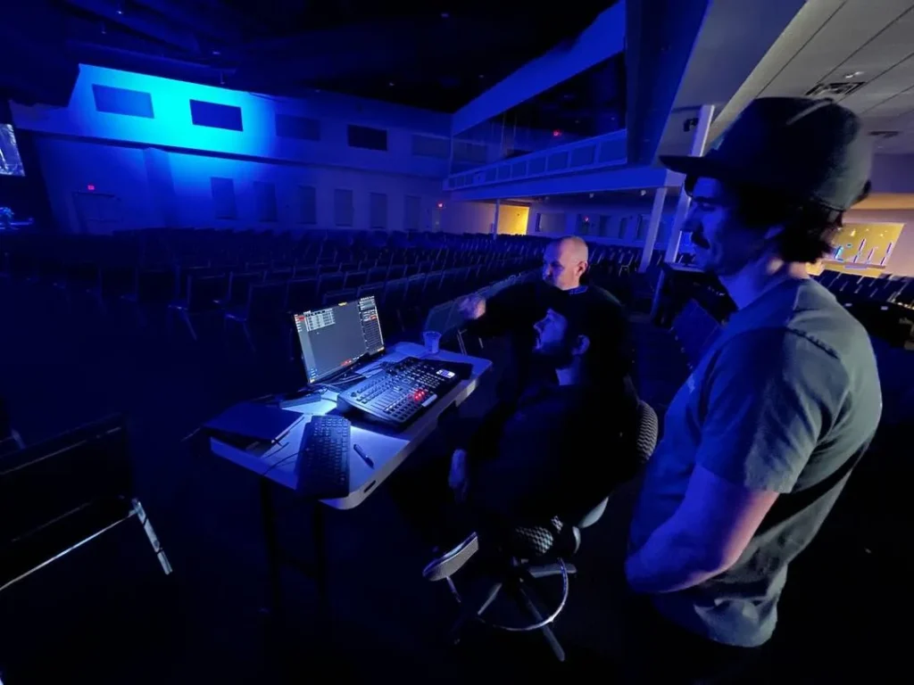 Three people working at a control desk in a dimly lit room.