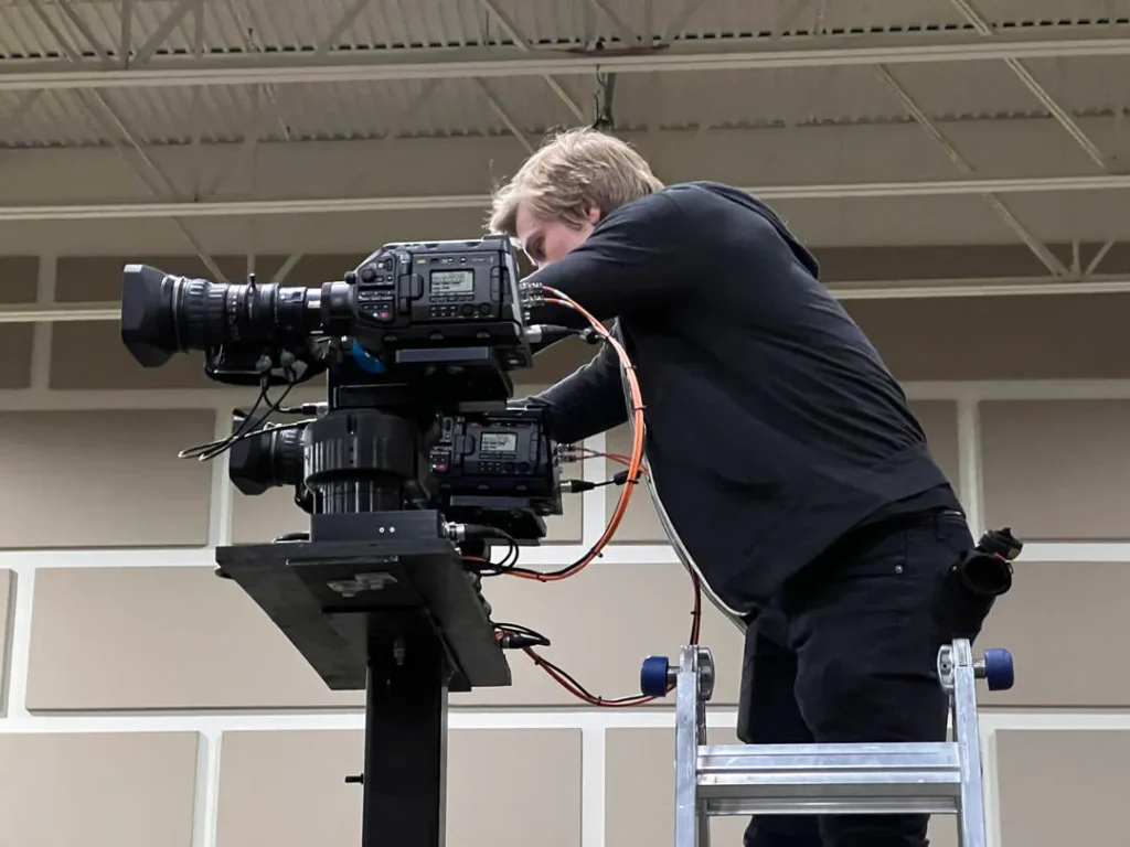 Person on a ladder adjusting a professional video camera setup.
