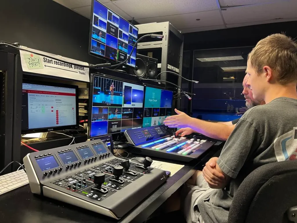 Two people operating video production equipment in a control room.